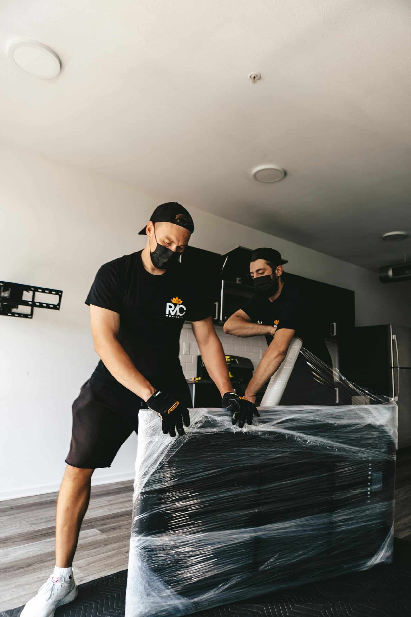 Two masked men moving a securely wrapped item in a modern room.